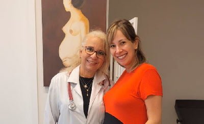 Dra. Greice Chetta sorrindo com uma paciente em seu consultório no Brooklin, São Paulo