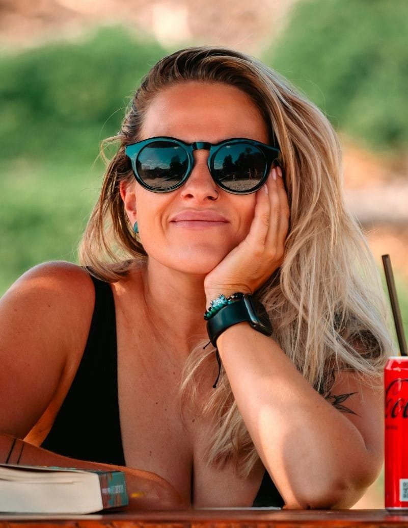 Mulher 45 anos feliz, sentada numa mesa com braço apoiando a cabeça.